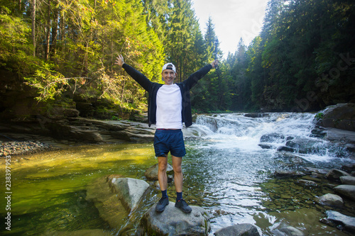 Young man walk near fast river in middle of forest