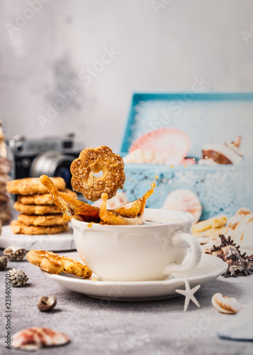 Cookie drops in cup of coffee with splash and biscuits, seashells and decorations. Dreams of sea vacation and concept. Copy space. © Iryna Melnyk