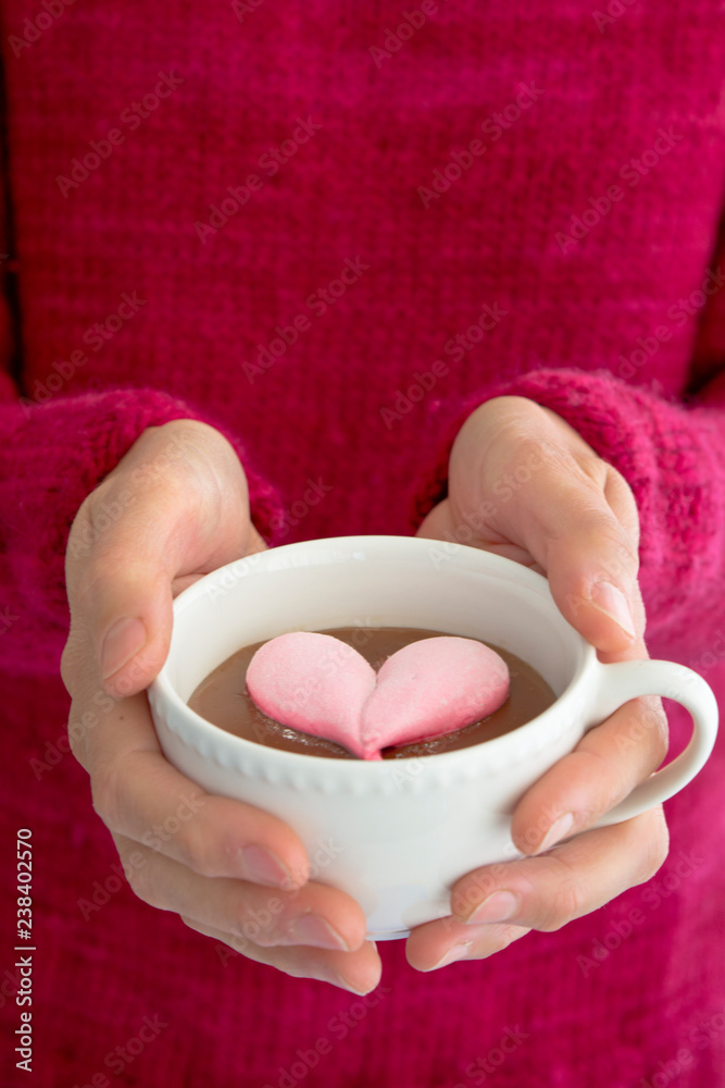 woman with magenta pullover holding white cup filled with hot chocolate with a pink heart-shaped marshmallow woman with magenta pullover holding white cup filled with hot chocolate with a pink heart-shaped marshmallow