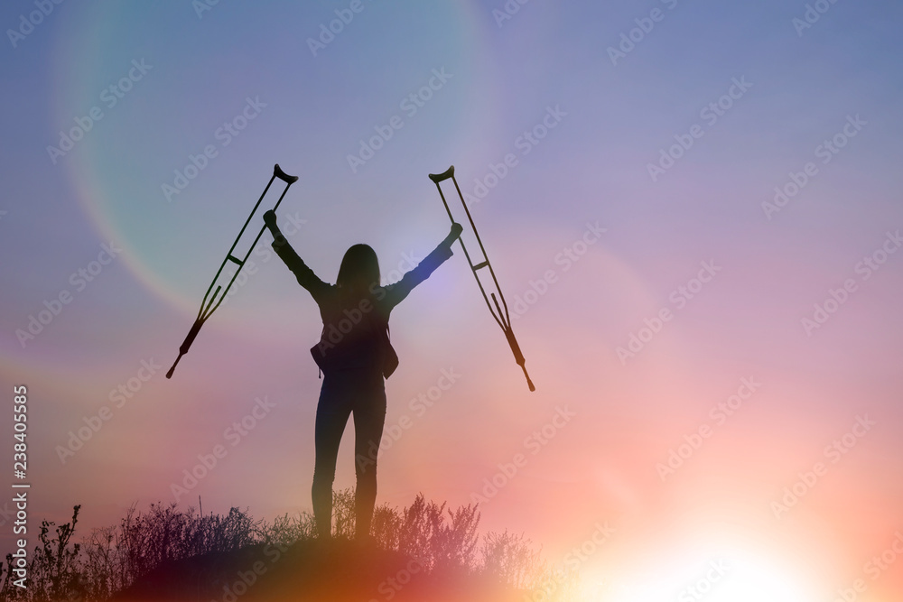silhouette of a girl on top of a mountain with crutches in her hands against the evening sky. victory, achievement, recovery.