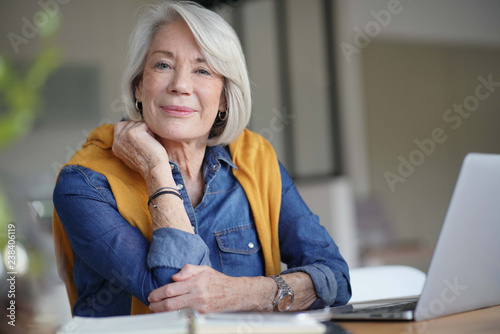  Beautiful senior woman looking pensive at home with laptop
