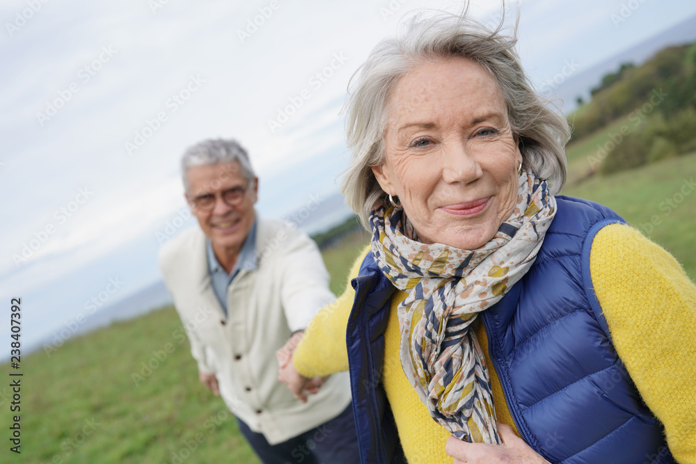Healthy senior woman holding husband's hand and leading way on countryside walk Healthy senior woman holding husband's hand and leading way on countryside walk