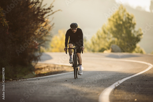 Professional road bicycle racer in action. Men cycling mountain road bike at sunset.
