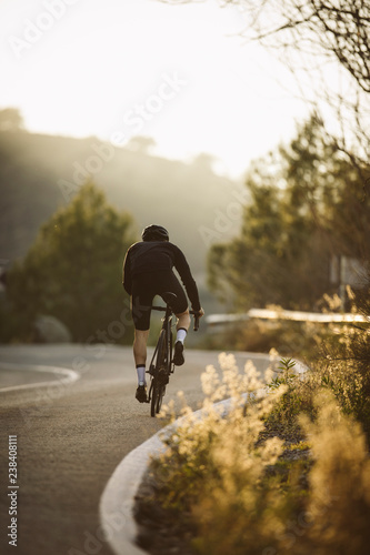 Fototapeta Naklejka Na Ścianę i Meble -  A side shot of a professional slim cyclist riding up a mountain