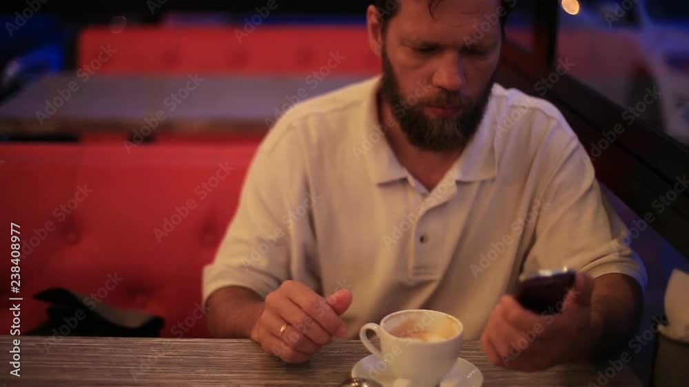 bearded man in a cafe drinking coffee and talking on the phone.
