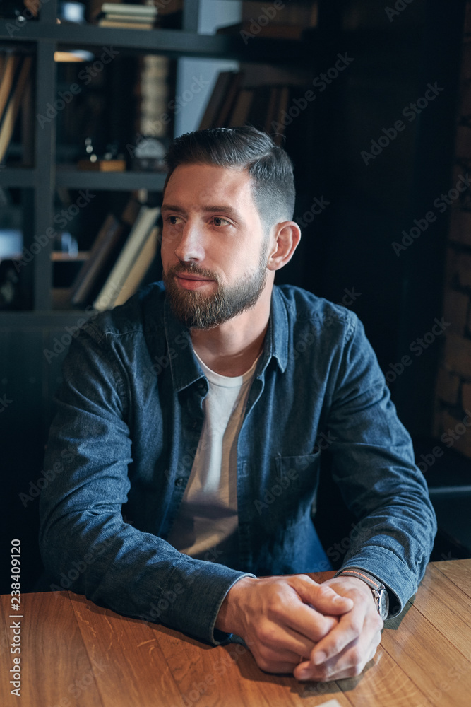 Young man sitting in a cafe at the table and waiting for the waiter with a menu to make an order Young man sitting in a cafe at the table and waiting for the waiter with a menu to make an order