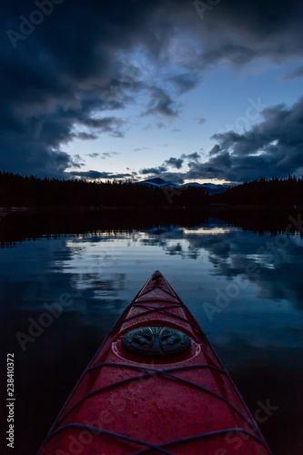 Kayaking in a peaceful and calm glacier lake during a vibrant cloudy sunset. Taken in Maligne Lake, Jasper National Park, Alberta, Canada.