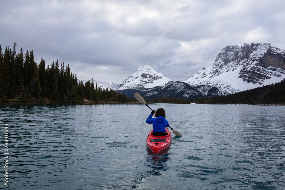 Adventurous girl kayaking in a glacier lake surrounded by the Canadian Rockies during a cloudy morning. Taken at Bow Lake, Banff, Alberta, Canada. Adventurous girl kayaking in a glacier lake surrounded by the Canadian Rockies during a cloudy morning. Taken at Bow Lake, Banff, Alberta, Canada.