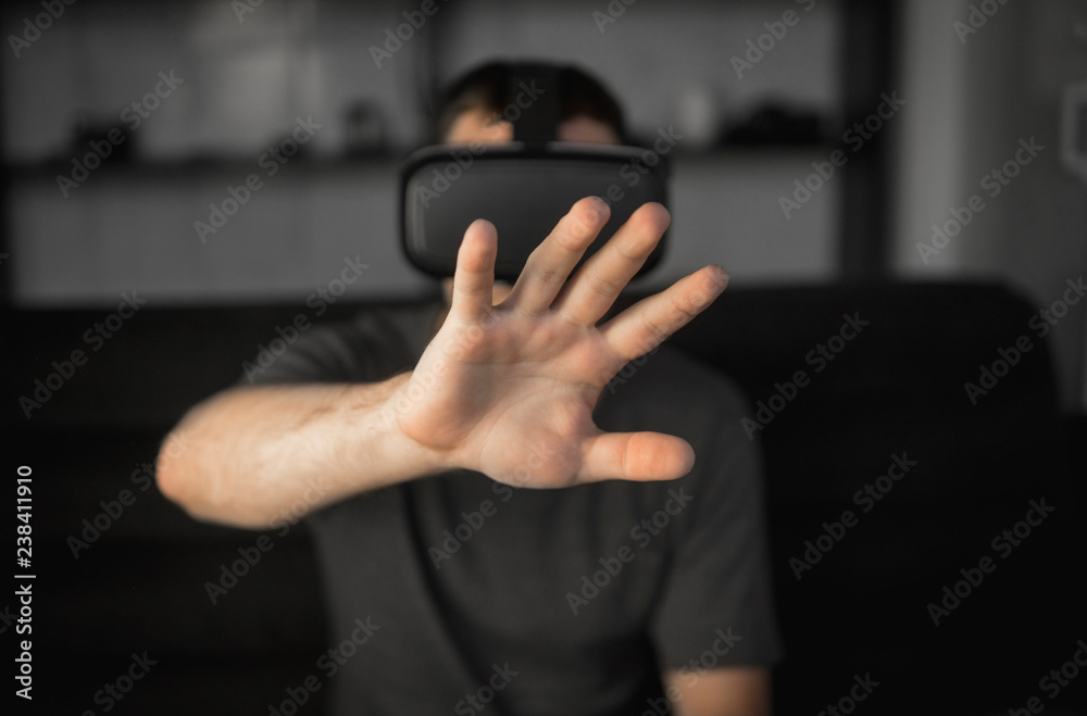 Young bearded man wearing headset of virtual reality in office sitting on a sofa and trying to touch something that he see in virtual world. Young bearded man wearing headset of virtual reality in office sitting on a sofa and trying to touch something that he see in virtual world.