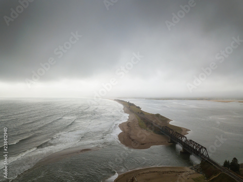 Aerial seascape view of train tracks running near a sandy beach during a dramatic cloudy day. Taken in Barachois, Quebec, Canada. photo