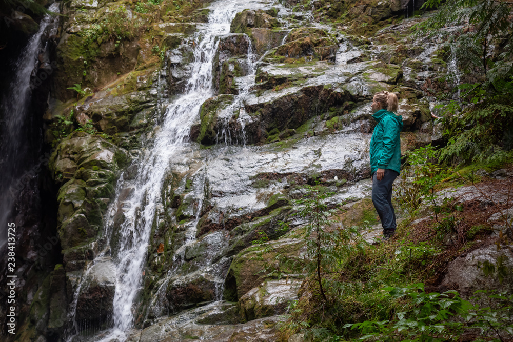 Adventurous female hiker is enjoying a beautiful view of a waterfall during a foggy day. Taken in Mt Fromme, North Vancouver, British Columbia, Canada.