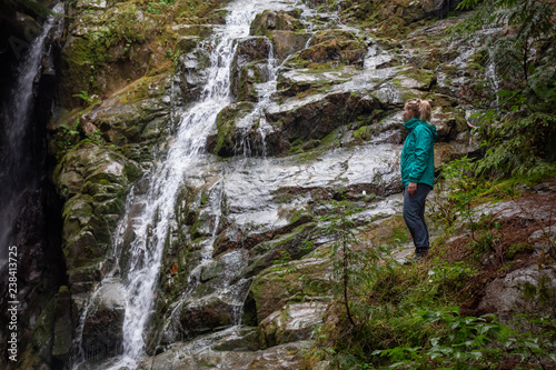 Adventurous female hiker is enjoying a beautiful view of a waterfall during a foggy day. Taken in Mt Fromme  North Vancouver  British Columbia  Canada.