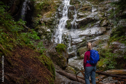 Adventurous female hiker is enjoying a beautiful view of a waterfall during a foggy day. Taken in Mt Fromme, North Vancouver, British Columbia, Canada.