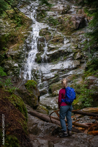 Adventurous female hiker is enjoying a beautiful view of a waterfall during a foggy day. Taken in Mt Fromme, North Vancouver, British Columbia, Canada.