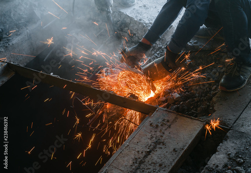 Male worker saws a disk grinding saw armature into a reinforced concrete panel, the destruction of the old house. Sparks from friction with metal. Rescue work.