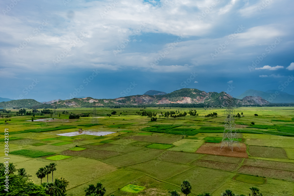 awesome top view of greenery grassland of paddy farm land with electric transmission pole, blue sky cloud mountain background.