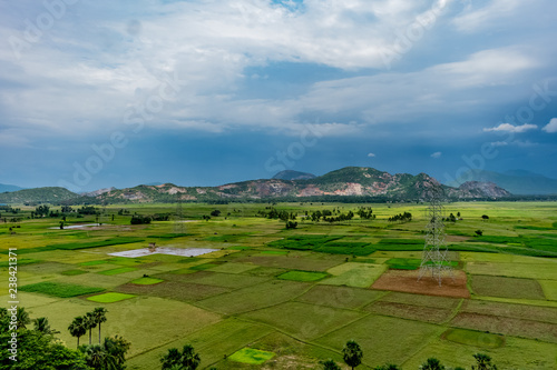 awesome top view of greenery grassland of paddy farm land with electric transmission pole, blue sky cloud mountain background. © Mayank