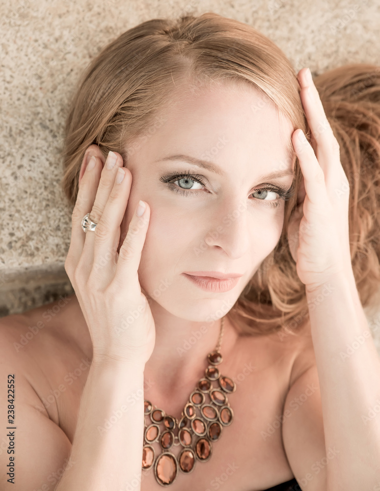 Obraz premium Closeup portrait of a beautiful woman lying and posing on the stairs and wearing a necklace on a sunny day.
