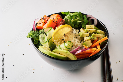 poke bowl with salmon, avocado, cucumber, arugula, broccoli, rice, carrot and sweet onions with chopsticks isolated over white background. side view