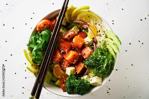 poke bowl with salmon, avocado, cucumber, arugula, broccoli, rice, carrot and sweet onions with chuka salad, chopsticks isolated over white background. top view close-up