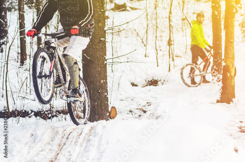 Bike rider flies through the air. Mountain biking on trails in a snowy forest. Extreme winter sport. photo