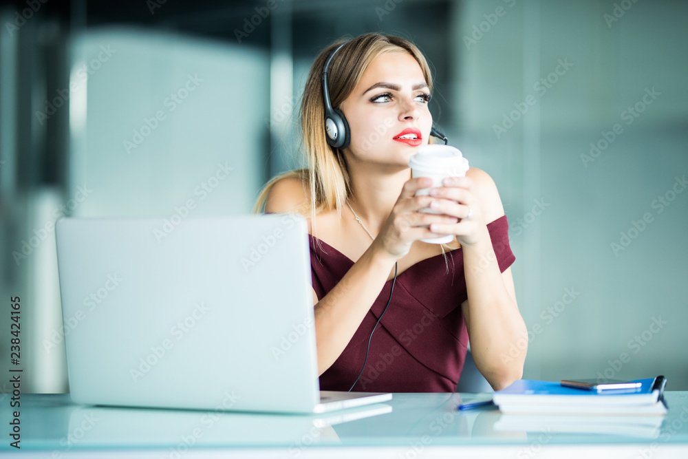 Happy young woman in headphones in call center and drinking coffee in office. Happy young woman in headphones in call center and drinking coffee in office.