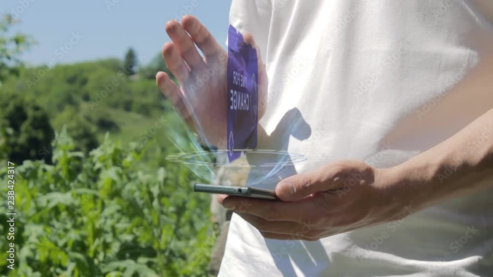 Man shows concept hologram Time for change on his phone. Person in white t-shirt with future technology holographic screen and green nature background Man shows concept hologram Time for change on his phone. Person in white t-shirt with future technology holographic screen and green nature background