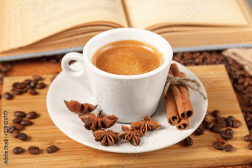 Coffee break a Cup of hot coffee and a book on a wooden table. A white Cup of black coffee surrounded by a small amount of roasted coffee beans, cinnamon, anise and an open book