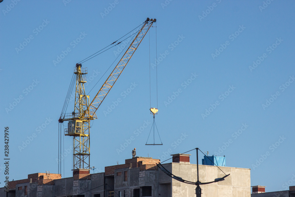 Construction site with yellow crane on blue sky background. Construction, construction work, lifting heavy loads up Construction site with yellow crane on blue sky background. Construction, construction work, lifting heavy loads up