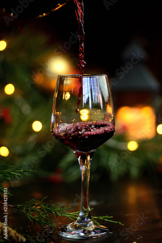 Red wine is being poured into a glass, against the backdrop of garlands and Christmas trees
