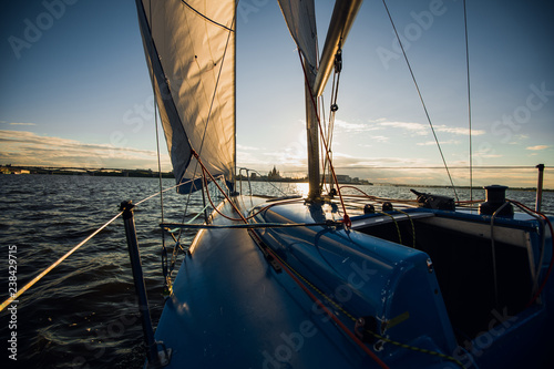 Sail boat with set up sails gliding in a sea or river at sunset