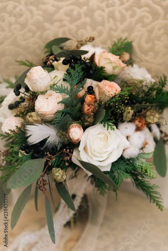 Winter bride's bouquet in pastel colors with roses, spruce, cotton, black berries, feathers and dried flowers rustic. Selective focus