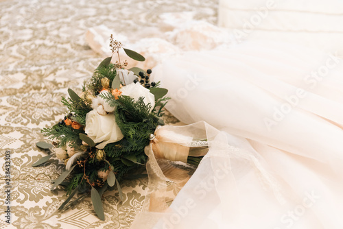 Quadro su tela Winter bride's bouquet with roses, cotton, spruce lies next to the wedding dress