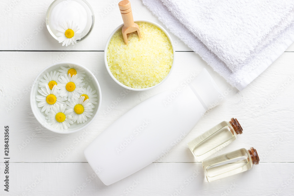 Spa background with bath yellow sea salt, natural cream and chamomile on white wooden table