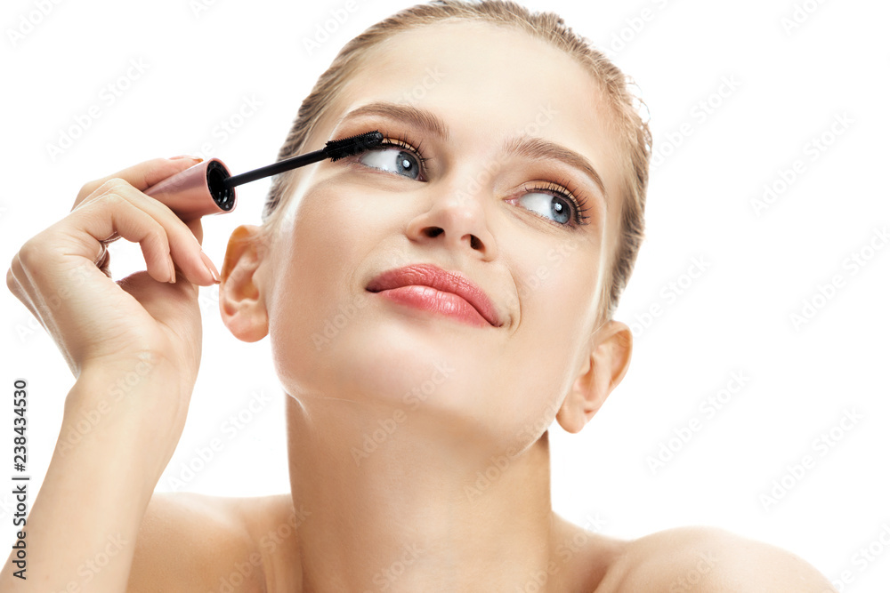 Pretty girl using black mascara on eyelashes. Portrait of girl finishing her makeup on white background. Youth and skin care concept