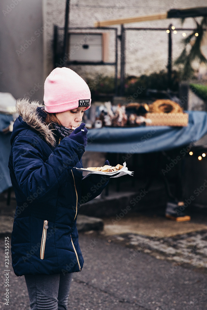 Young girl eating freshly prepared crepes which are thin pancakes with chocolate spread filling outside at Christmas market. Popular warm street food in Switzerland especially in winter time. Swiss fo
