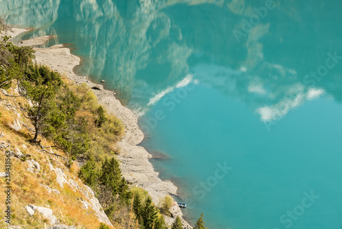 Aerial autumn view in sunny day on beach Oeschinensee mountain lake with pine trees and snowed mountains reflections in turquoise water, Kandersteg, Switzerland