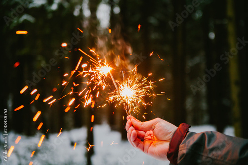 Sparklers hand men. snowy forest background.
