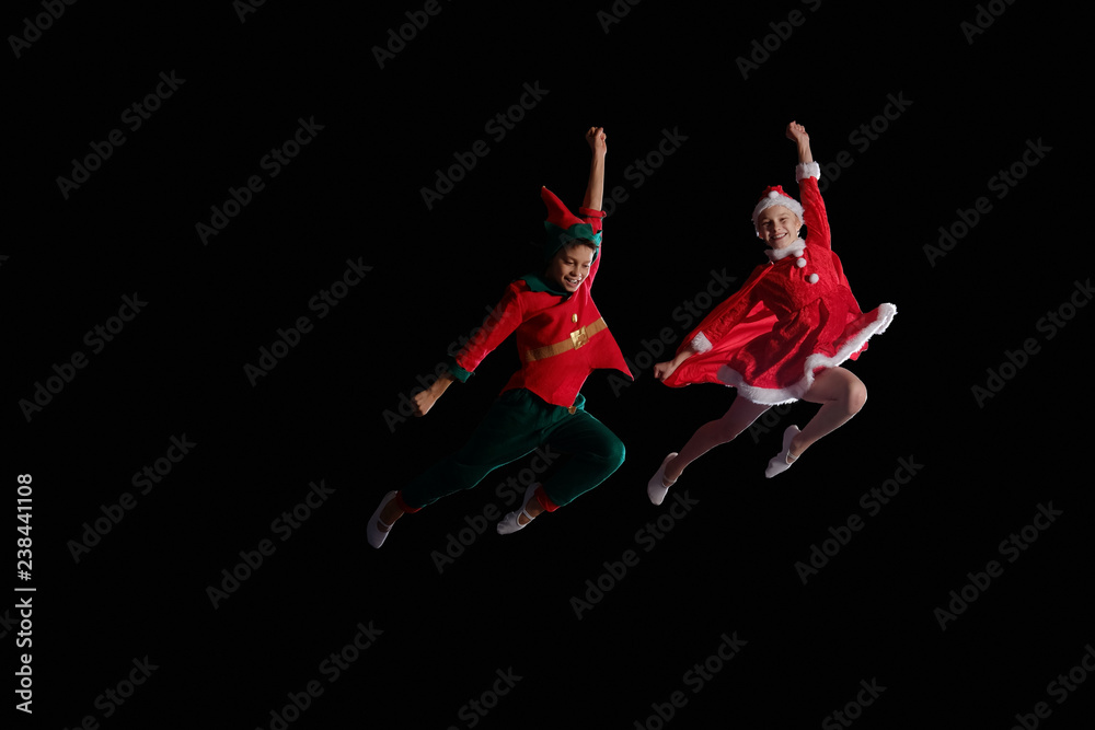 Christmas time, childhood, fairy tale. Cheerful kids - A young girl wearing a Santa's costume and boy wearing elf costume flying together