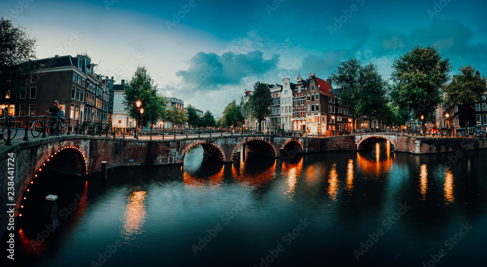 Evening twilight panorama of Amterdam cityscape with canal, bridge and medieval houses in the evening illumination. Bridge over Keizersgracht (Emperor's canal) in Amsterdam, The Netherlands