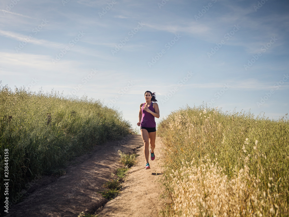 Mid adult woman jogging on path through field Mid adult woman jogging on path through field