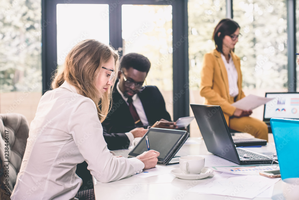 Businesspeople Having Meeting In Modern Office. Focus on pretty blond woman writing, African-American man and Caucasian woman on the background Businesspeople Having Meeting In Modern Office. Focus on pretty blond woman writing, African-American man and Caucasian woman on the background