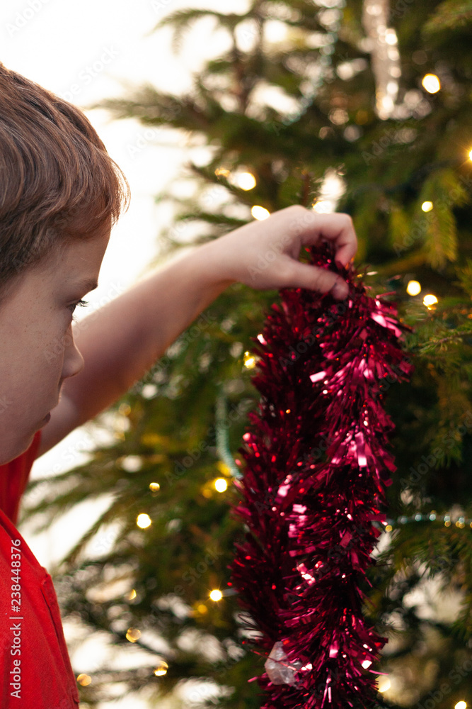 A young boy decorating a Christmas tree with red tinsel