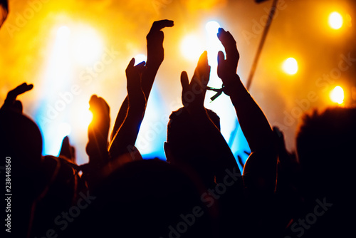 silhouettes of concert crowd in front of bright stage lights. cheering crowd of people with hands up on popular rock music concert. Dark background, smoke, concert spotlights.