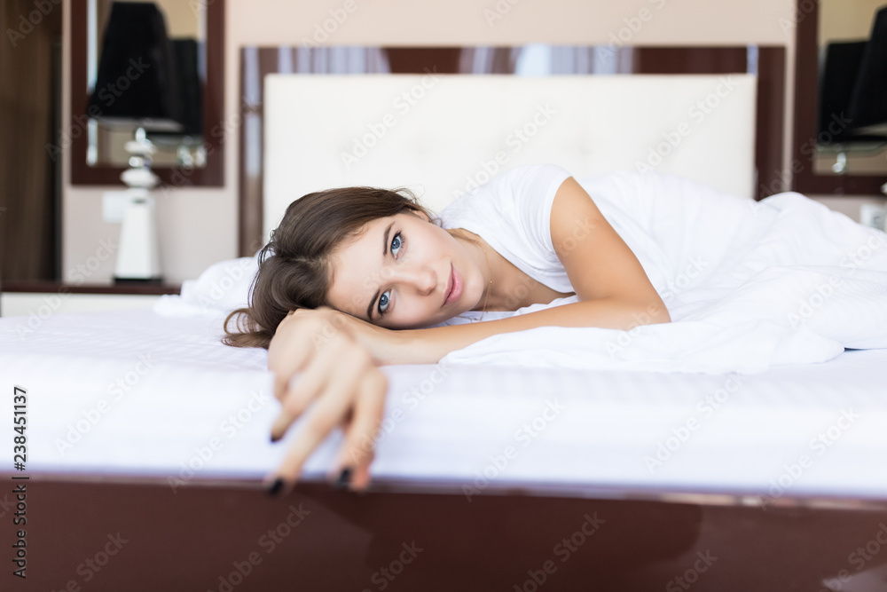 Young woman lying at the end of the bed looking forward while smiling. Young woman lying at the end of the bed looking forward while smiling.