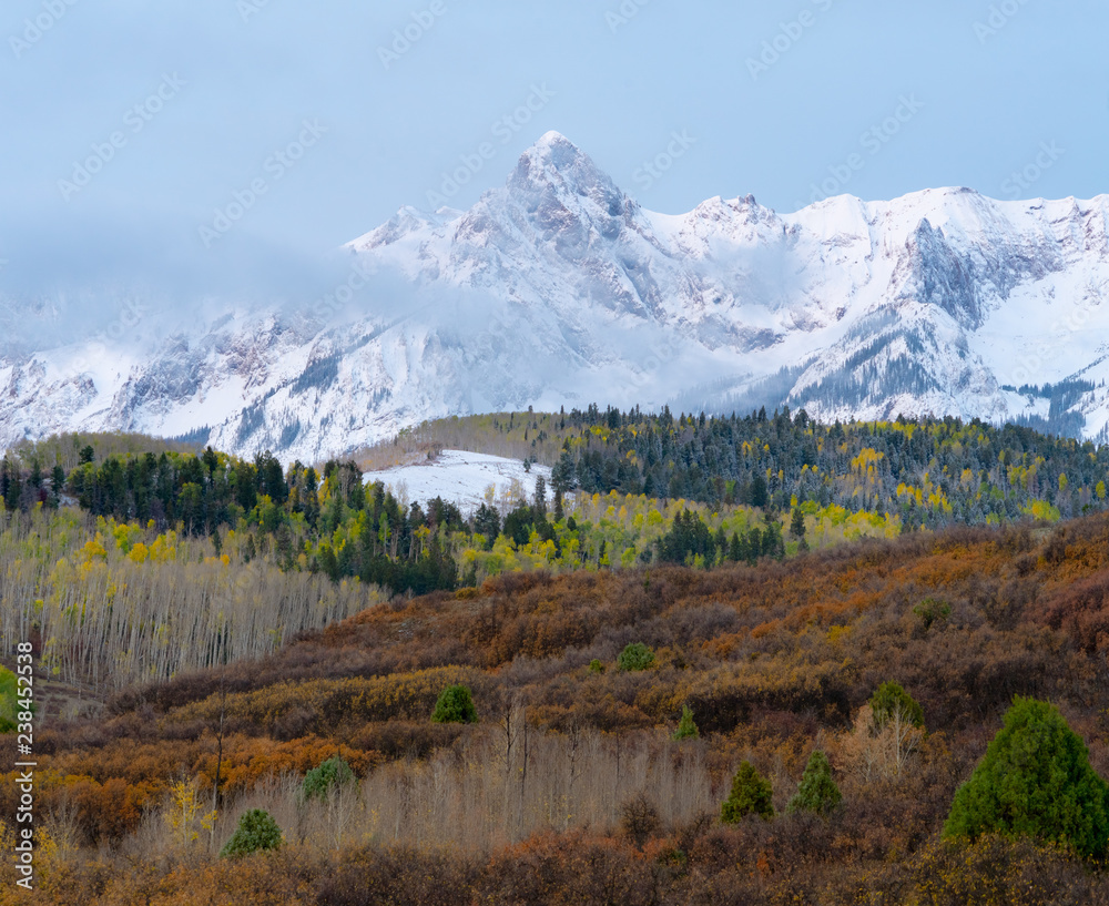 White snow capped peaks tower above dusted fall colored trees White snow capped peaks tower above dusted fall colored trees