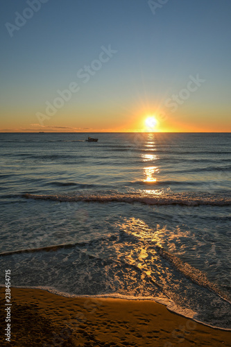 Sea sunrise from a sandy beach with a boat and water reflections, Alassio, Liguria, Italy