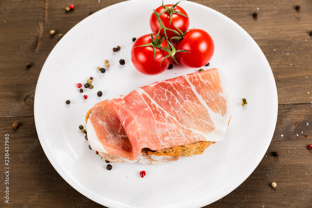 Slice of bread with preserved ham and ingredients. White plate on a wooden background Slice of bread with preserved ham and ingredients. White plate on a wooden background