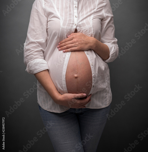 Pregnant girl with a bare belly on gray background.