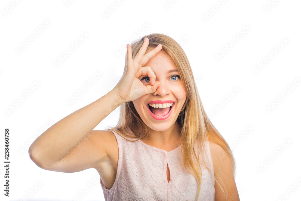 Young beautiful blonde woman shows okay near her eyes and smiles enthusiastically with her mouth open, close-up shot on an isolated background Young beautiful blonde woman shows okay near her eyes and smiles enthusiastically with her mouth open, close-up shot on an isolated background